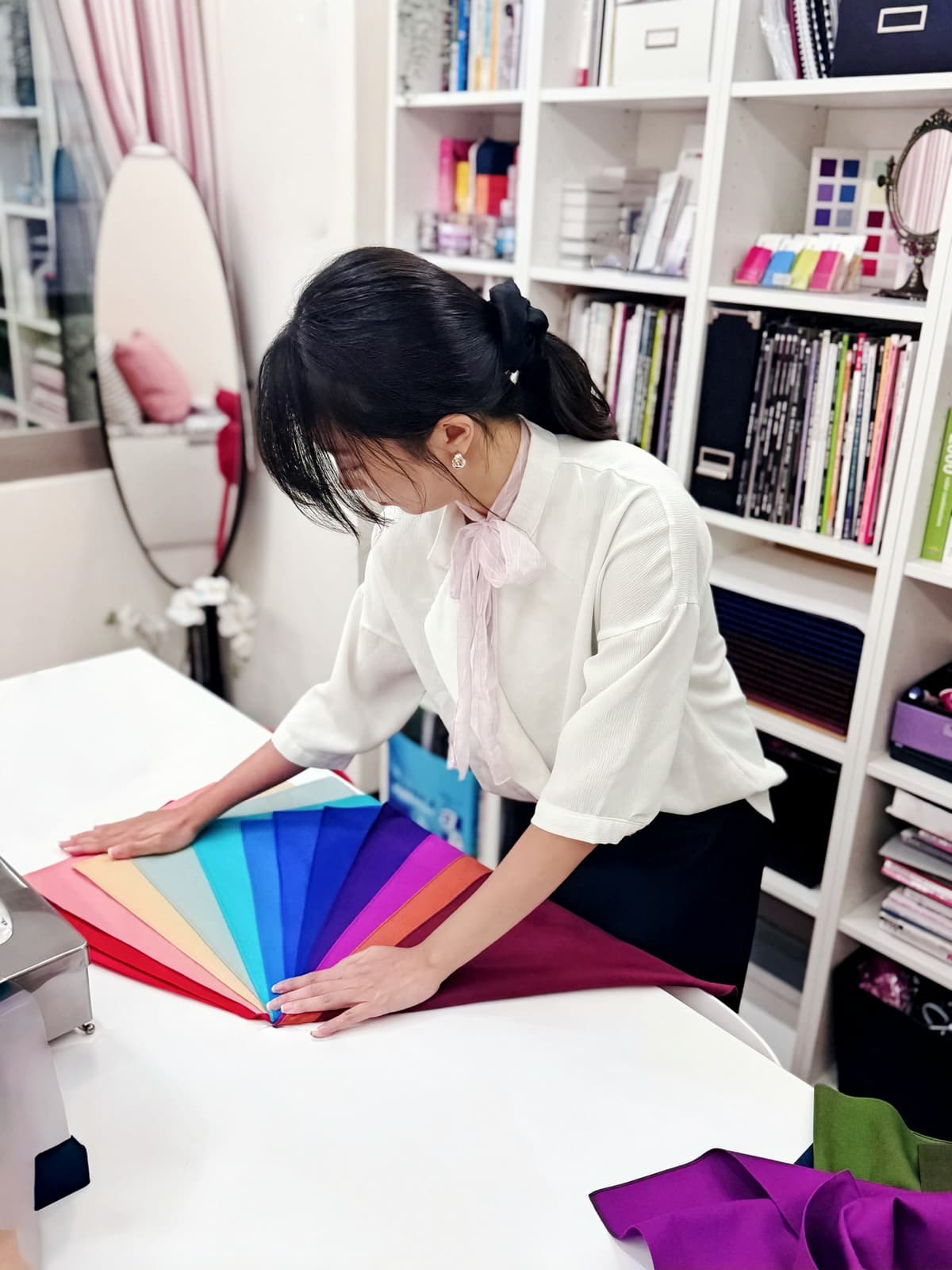 Tanya arranging a rainbow color fan on her studio desk, surrounded by color reference books